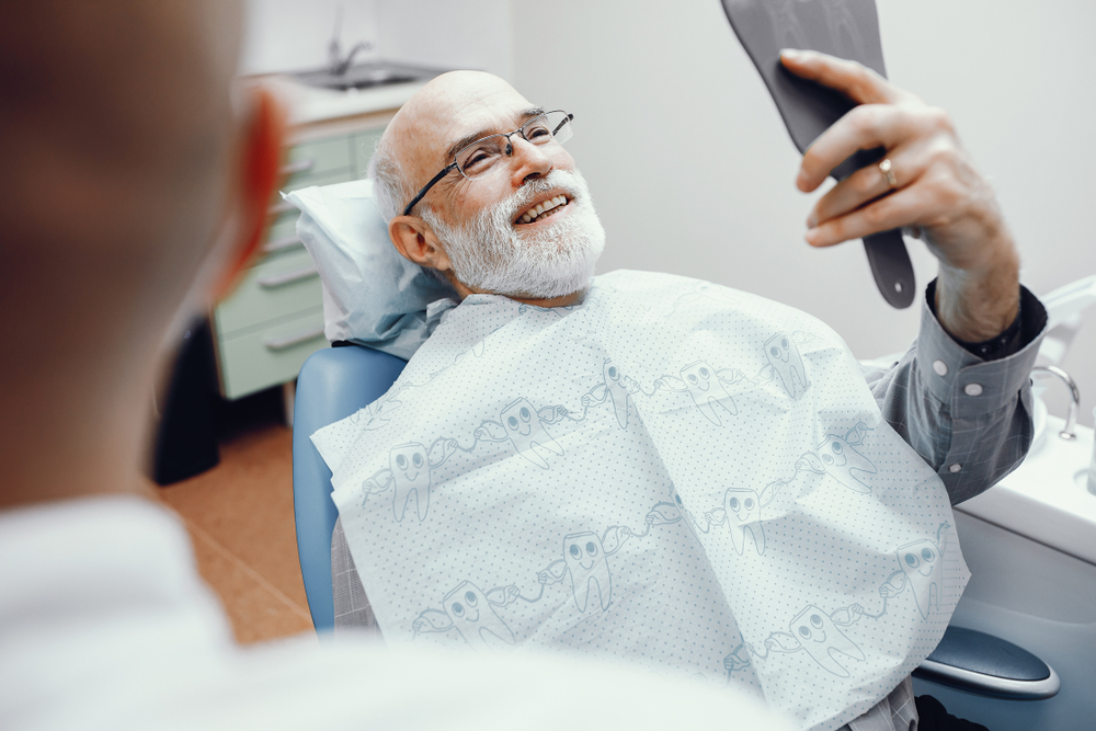 an older man looks in the mirror after his dental hygiene and cleaning appointment. 